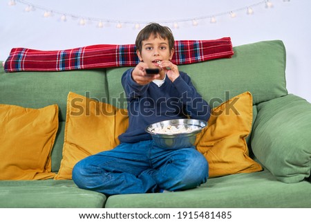 A Emotional child watching tv on the sofa and eating popcorn at home, free space