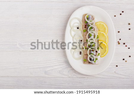 Pickled fillet fish herring, onions, lemon on white plate. Space for text