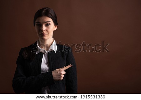 Portrait of serious brunette business woman pointing her finger to the side in studio on brown background with copyspace