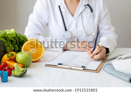 Female nutritionist doctor writing vegetable diet plan Royalty-Free Stock Photo #1915531801