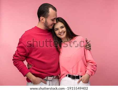 Photo of sweet couple hug each other and smile. Male and female are in love, isolated over pink background