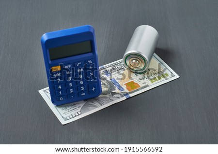 Old batteries, calculator and banknote of one hundred dollars on dark concrete desk. Recycling concept. Save environment. cost, purchase or sale of electricity