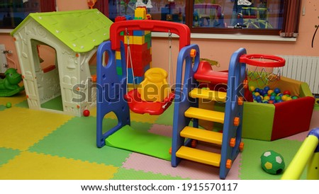 Toy house, swing, children's slide and dry pool with colored balls in interior of modern kids playing room in the kindergarten - children's entertainment, recreation, sports, educational games indoor Royalty-Free Stock Photo #1915570117