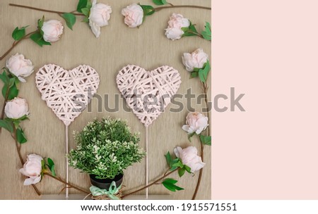 Decorative braided hearts on a natural background surrounded by delicate roses and a green plant, close-up, top view, white and green on beige