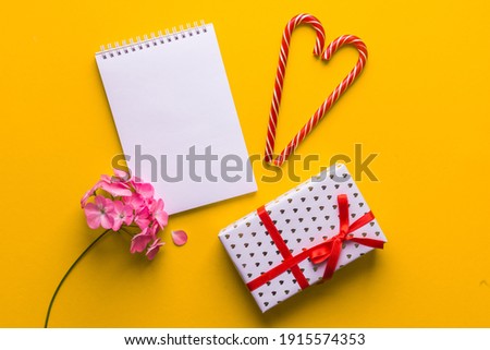 minimal set with blank notepad, gift box with red bow, pink flower, lollipop caramel cane. Christmas, new year, black friday sale, birthday concept. top view, copy space, place for text, flat lay
