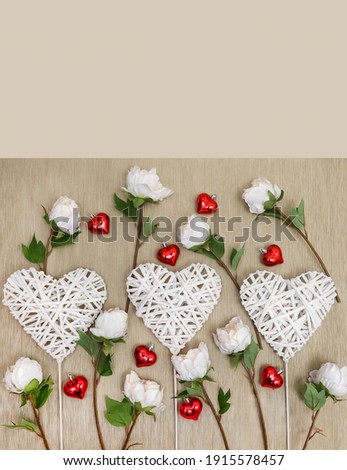 Decorative braided hearts on a natural background surrounded by delicate roses and small shiny hearts, close-up, top view, white, red and green on a beige background