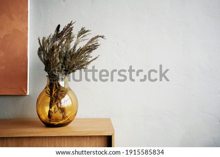 a bouquet of dried flowers stands in a transparent stylish designer vase of gold color. decoration of the interior. copy space. background grey wall