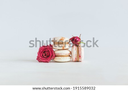 Tasty french macaroons with pink roses on a white wooden background. Place for text.