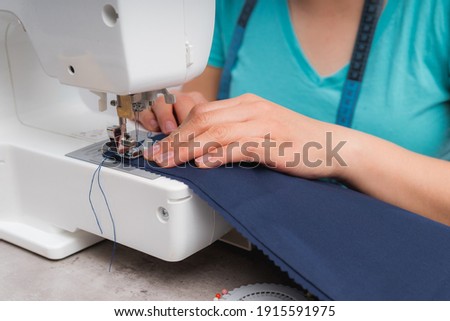 Cheerful woman sewing while sitting at her working place in fashion workshop Royalty-Free Stock Photo #1915591975