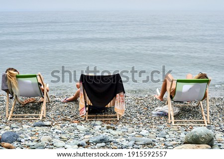 Girls on deck chairs on a pebble beach by the Aegean Sea in Greece
