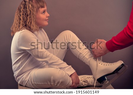 girl with skates. child in white clothes. fine hair. winter sports. hands tie the laces.