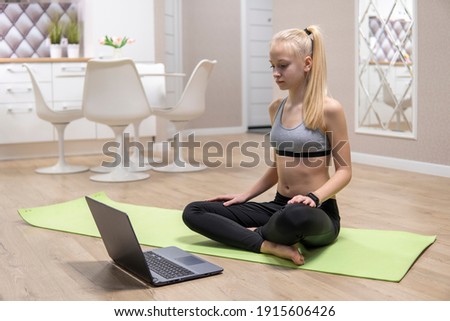 young attractive girl is engaged in fitness at home and looks at the laptop. quarantine fitness concept. high quality
