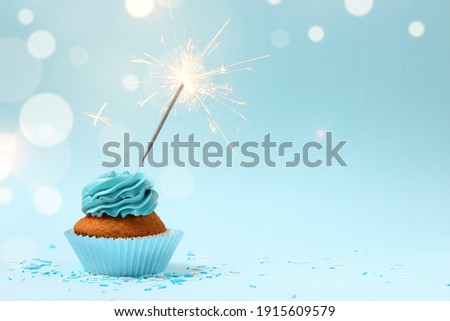 Cupcake with cream and burning sparkler for a birthday or other holiday with a shopping plan on a colored background with bokeh lights 