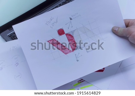 Creative workplace of a Graphic Designer. A man in the office is developing a logo on the table against the background of printed sketches and a laptop