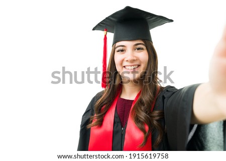Personal perspective of a gorgeous young woman in a black gown taking a selfie with a camera during her graduation ceremony 