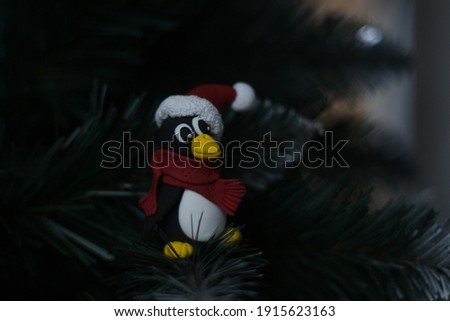 new year penguin in a santa claus  hat with pompon and red scarf sits on the christmas tree and stares intently