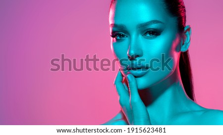 High fashion model metal silver lips and face woman in colorful bright neon UV blue and purple lights, posing in studio, beautiful girl, glowing makeup, colorful makeup. Glitter Bright Neon Makeup Royalty-Free Stock Photo #1915623481