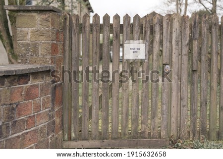 Old wooden gate with sign which reads shut the gate. Rotting wood along the bottom.