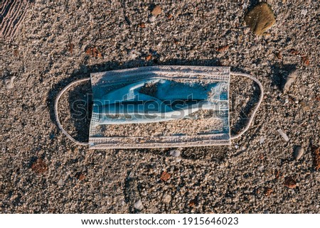 A surgical mask lying on a sandy floo