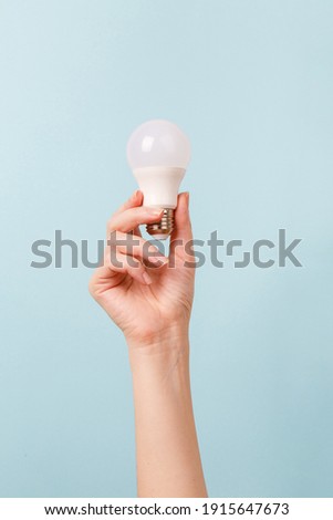 Hand holding a LED light bulb on blue background. Using economical and environmentally friendly light bulb concept. Idea. Energy saving lamp in woman's hand Royalty-Free Stock Photo #1915647673