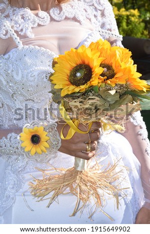 the bride's hands with gold rings are holding a bouquet of yellow sunflower flowers