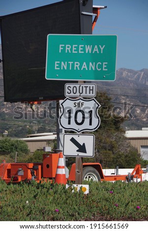 Freeway entrance sign with additional information and roadwork signage equipment in the background