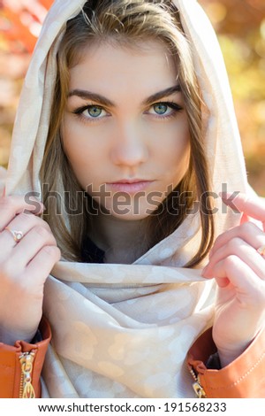 Beautiful young woman wearing ivory shawl on autumn outdoors day looking at camera closeup picture