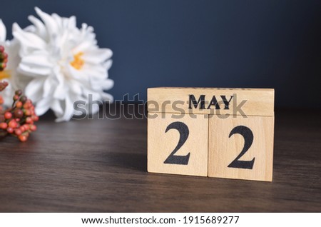 May 22, Date cover design with calendar cube and white Paeonia flower on wooden table and blue background.