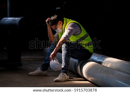 Worker wearing uniform sitting in factory plantation posing feel tried and serious with work ,he wearing face mask to protect pollution and virus. Royalty-Free Stock Photo #1915703878