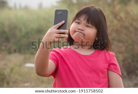 Happy portrait fat girl Asian cute cheeks with black hair wearing red-pink shirt. Taking a picture with smartphone with a bright smile In evening at sunset At the front garden with Twilight of the day