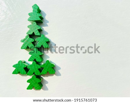 Green color resemble Christmas tree formation of green board game meeples pieces on white color wood table with empty copy space of white background for text , quote usage in holiday theme,in Thailand