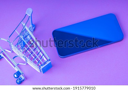 An empty shopping cart and a modern smartphone on a red scarlet background. Shopping, online shopping concept, copy space, top view, scarlet background, purple tinting