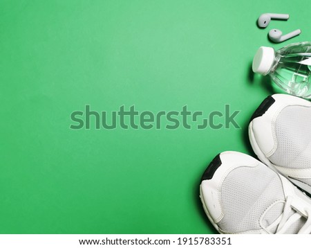 Healthy life concept. Top view on green background with sport shoes, water bottle and earbuds. 
