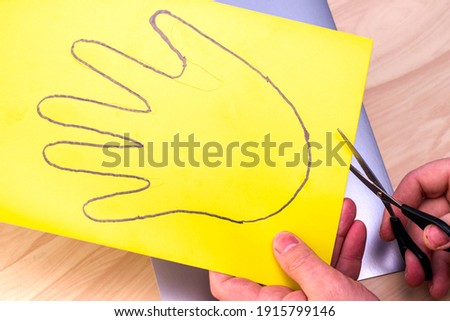 making the simplest Easter bunny with your own hands man with scissors cut out the circled hand on yellow paper. High quality photo