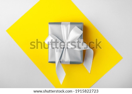 Trendy attractive minimalistic gift on the yellow and gray background. Colors of 2021. Merry Christmas, St. Valentine's Day, Happy Birthday and other holidays concept.