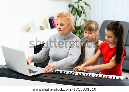 grandmother and granddaughters learn to play the piano synthesizer on a laptop online at home