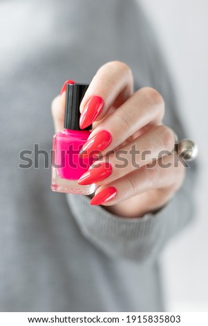 Female hand with long nails and a bottle bright neon pink red color nail polish