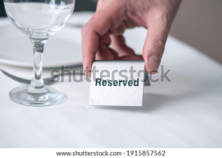 A waiter holding iron sign with text reserved on table with white tablecloth at restaurant