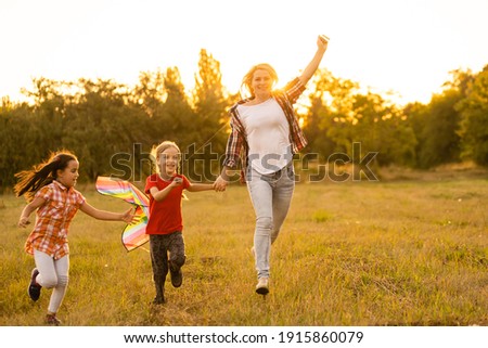 happy family mother and children run on meadow with a kite in the summer on the nature