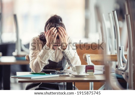 Female busines owner holds her head in hands in desperation over paperwork and tax declaration in a closed pub.