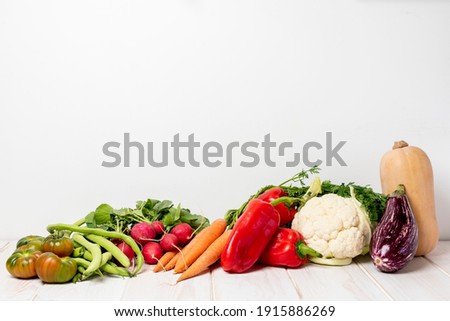 Tomatoes, radishes, 
broad beans, carrots, peppers, cauliflower, butternut squash and eggplant on a white wooden table and white background. Vegetables still life.
