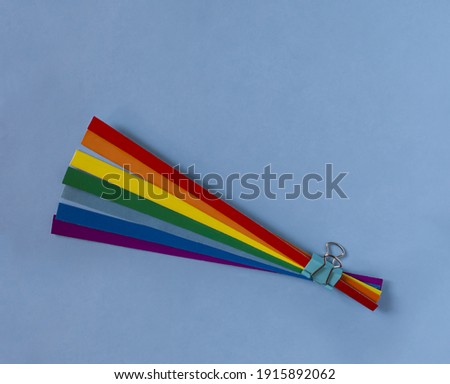 Rainbow bouquet. Strips of rainbow colored paper are held together with a paper clip. Light blue background.