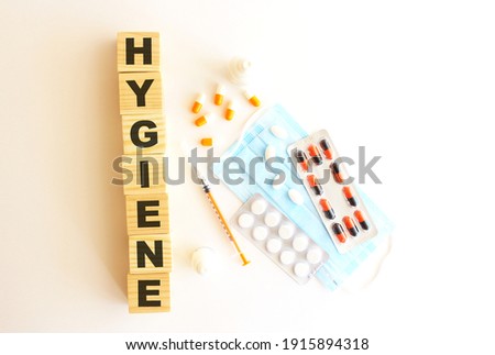 The word HYGIENE is made of wooden cubes on a white background with medical drugs and medical mask.