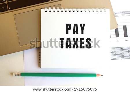 Notepad with the text PAY TAXES is on the laptop keyboard. Minimal work space.