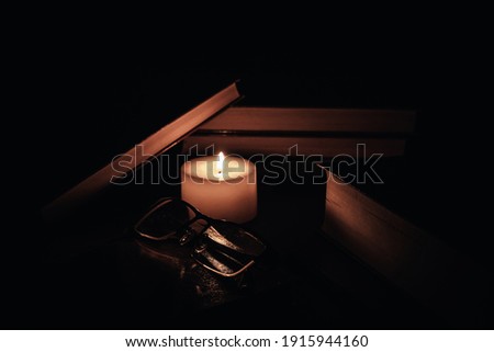 books illuminated by candlelight, reading glasses on top of them, a soft atmosphere, a book day concept.