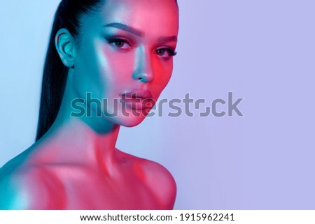 High fashion model metal silver lips and face woman in colorful bright neon UV blue and purple lights, posing in studio, beautiful girl, glowing makeup, colorful makeup. Glitter Bright Neon Makeup Royalty-Free Stock Photo #1915962241