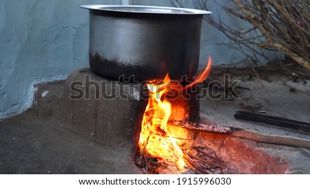 Illuminating reddish wooden fire in clay stove in traditional Indian kitchen. Red flamings of fire in brick stove with Aluminium pan.