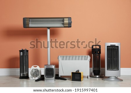 Different electric heaters near orange wall indoors Royalty-Free Stock Photo #1915997401