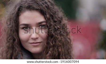 Close-up portrait of a young woman with curly hair posing on a city street on a cold winter day.
