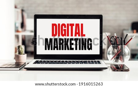 Laptop with DIGITAL MARKETING text on modern office background.